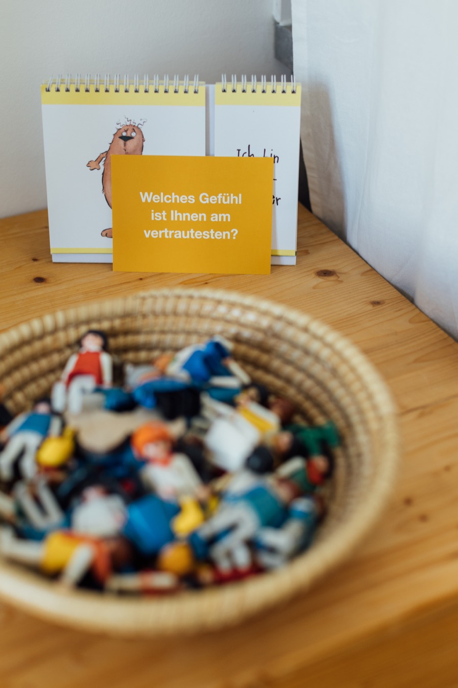 Korb mit Spielfiguren und eine Karte mit der Frage &bdquo;Welches Gef&uuml;hl ist Ihnen am vertrautesten?&ldquo;
