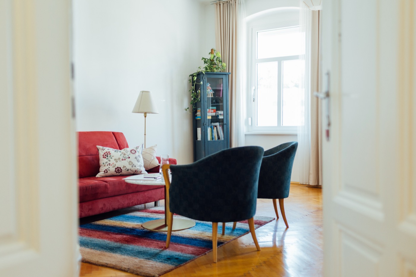 Blick durch die T&uuml;r in den Praxisraum mit rotem Sofa und zwei Sesseln