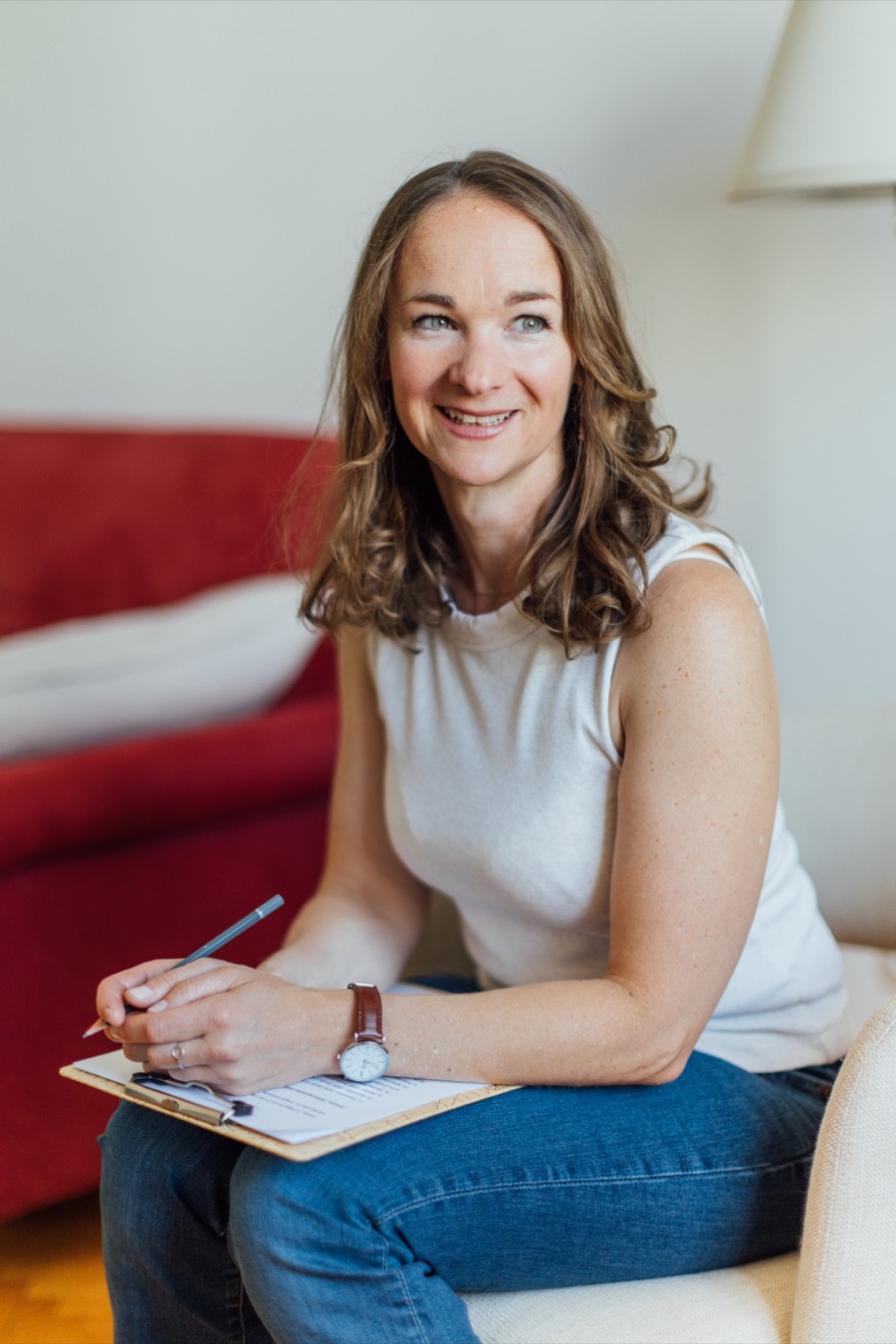 Katharina Pichler mit Notizblock vor dem roten Sofa ihrer Praxis