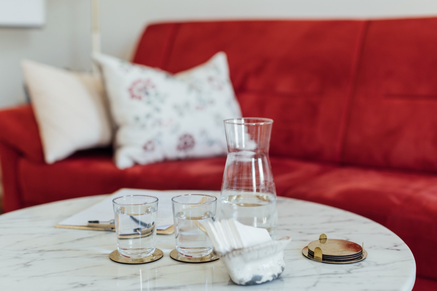 Couchtisch mit Karaffe und Gl&auml;sern vor dem roten Sofa im Praxisraum